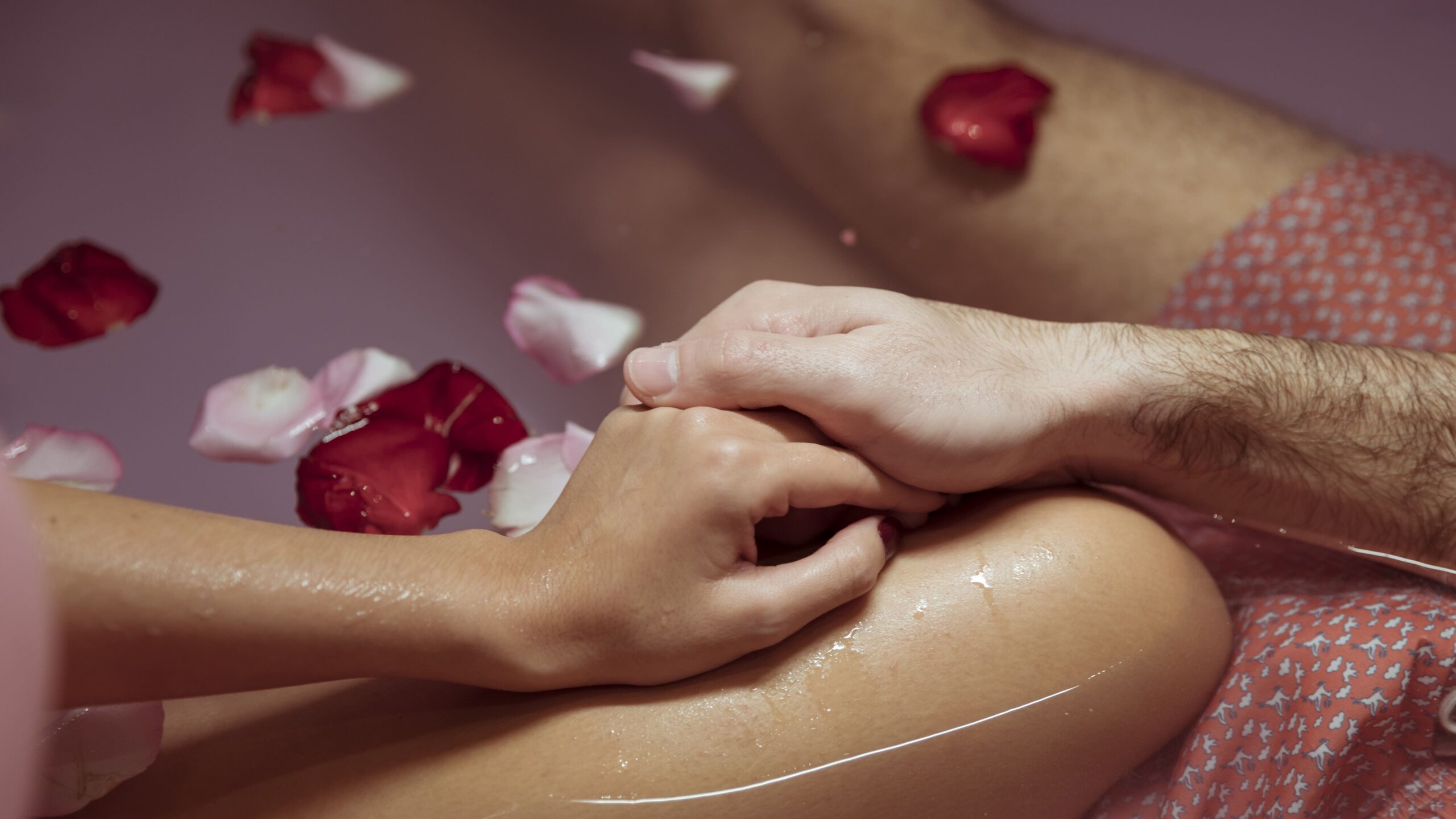 Couple holding hands in a private in-room hot tub surrounded by floating rose petals